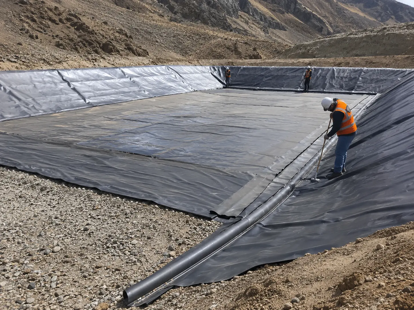 Cuadrilla con casco y chaleco desplegando geomembrana en una poza de solución, con una tubería HDPE tendida sobre el talud