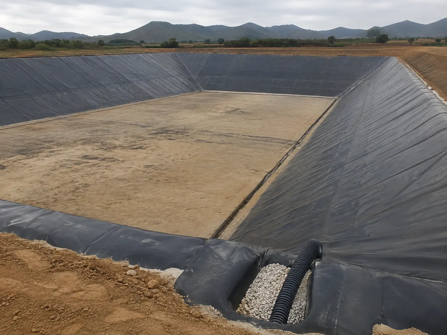 Poza de relaves revestida con geomembrana HDPE en los taludes, con una zanja de grava y tubería corrugada de drenaje al pie